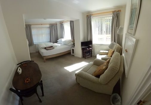 Image shows bedsitting room with double bed, 2 armchairs, tv and dining table and 2 chairs